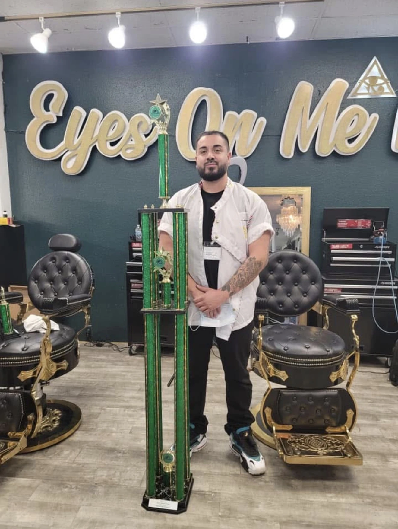 Q.tha_barber standing with a barber competition trophy